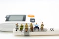 Miniature people sitting on glucose meter with lancet. Image use