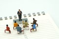 Miniature people sitting on red staples placed on a Book Rankings list. meeting or Discussion using as background business conce