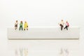 Miniature people, sitting on white block and read book. White block can write anything for various occasions Royalty Free Stock Photo