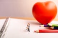 Small couple figures in love standing on notebook and red heart.