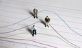 Miniature people standing on linear graphs. Royalty Free Stock Photo