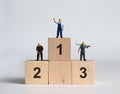 Miniature people standing on top of the ranked wooden blocks.