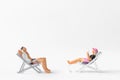 Miniature people sunbathing on deck chairs on white background