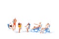 Miniature people sunbathing on deck chairs on white background