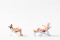 Miniature people sunbathing on deck chairs on white background