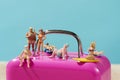 Miniature people in swimsuit on a pink suitcase