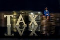 Miniature People. Tax concept.Word Tax and taxman sitting on stacked coins.. Macro Royalty Free Stock Photo