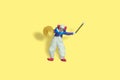 Miniature people toy figure photography. Full body of a bald clown holding crash cymbal and stick. Isolate on yellow background