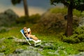 Miniature people toy figure photography. Girl seat on deck chair reading a book, relaxing at garden Royalty Free Stock Photo