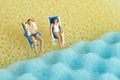 Miniature people toy figure photography. Men and girl relaxing at beach chair in front of wavy beach Royalty Free Stock Photo