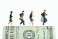 Miniature people toy figure photography. School admission budget concept. Pupils running above rolled dollar money paper cash,