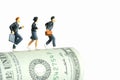 Miniature people toy figure photography. School admission budget concept. Pupils running above rolled dollar money paper cash,