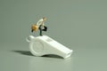 Whistle blower concept. A businessman running above white whistle, isolated on grey background