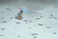 Miniature people toy figure photography. A woman wearing a raincoat using umbrella, walking on the street during a storm, against