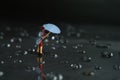 Miniature people toy figure photography. A woman wearing a raincoat using umbrella, walking on the street during a storm, against