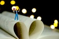 Miniature people toy photography. Poem and poetry concept. Boy standing above opened book, express his love holding heart shape.