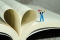Miniature people toy photography. Poem and poetry concept. Boy standing above opened book, express his love holding heart shape