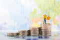 Miniature people: traveller couple figure standing on top of stack coins using as background retirement planning concept