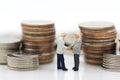 Miniature people : Two businessmen make a deal, with stack of coins to background, using as commitment, agreement, saving, finance