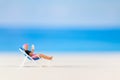 Miniature people , a woman relaxing on a deck chair and reading a book Royalty Free Stock Photo