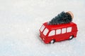 A miniature red bus carries Christmas tree on white snow background. festive Christmas mood