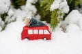 A miniature red bus carries Christmas tree on white snow background. festive Christmas mood