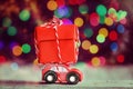 Miniature Red Car Carrying a big red box on colorful bokeh background. Holiday Merry Christmas concept