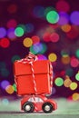 Miniature Red Car Carrying a big red box on colorful bokeh background. Holiday Merry Christmas concept.