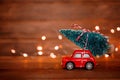 Miniature red car toy delivering christmas tree on wooden background with light. Christmas greeting card concept. Close up Royalty Free Stock Photo