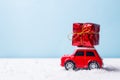 Miniature red car toy delivering gift box on blue background. Christmas greeting card concept Royalty Free Stock Photo