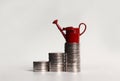 A miniature red watering can on a pile of three stepped coins.