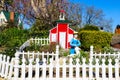 A miniature red and white house with a clay statue of a woman in a blue dress with a white picket fence