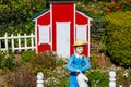 A miniature red and white house with a clay statue of a woman in a blue dress with a white picket fence