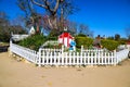 A miniature red and white house with a clay statue of a woman in a blue dress with a white picket fence