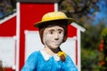 A miniature red and white house with a clay statue of a woman in a blue dress with a white picket fence