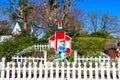 A miniature red and white house with a clay statue of a woman in a blue dress with a white picket fence