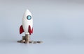 Miniature rocket stand on stack of coins, rocketship as symbol to open business project