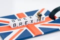 Miniature sad man sit on cube block with alphabets building the word BREXIT on union jack UK flag with white copy space background Royalty Free Stock Photo