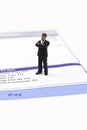 Miniature scale model businessman standing on a wage pay slip showing earnings deductions.