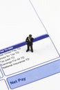 Miniature scale model businessman standing on a wage pay slip showing earnings deductions.