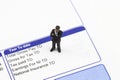 Miniature scale model businessman standing on a wage pay slip showing earnings deductions.