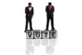Miniature scale model politicians standing behind the word vote