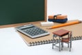 Miniature school desk, chalkboard and calculator on white background.