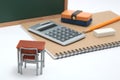 Miniature school desk, chalkboard and calculator on white background.