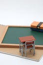 Miniature school desk, chalkboard and notebook on white background.
