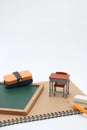 Miniature school desk, chalkboard and notebook on white background.