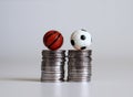 A miniature soccer ball and a basketball ball on a pile of coins.