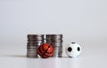 A miniature soccer ball and a basketball ball with pile of coins.