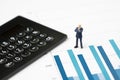 Miniature success and confidence businessman in suit standing on performance bar graph with black calculator using as work report Royalty Free Stock Photo