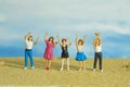 Miniature tiny people toys photography. Group of teens raised hand or hands up celebration at the beach